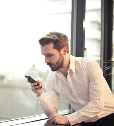 A man uses a smartphone while leaning beside a window