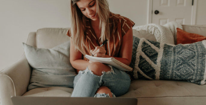 A woman sitting on a sofa writing on a notepad